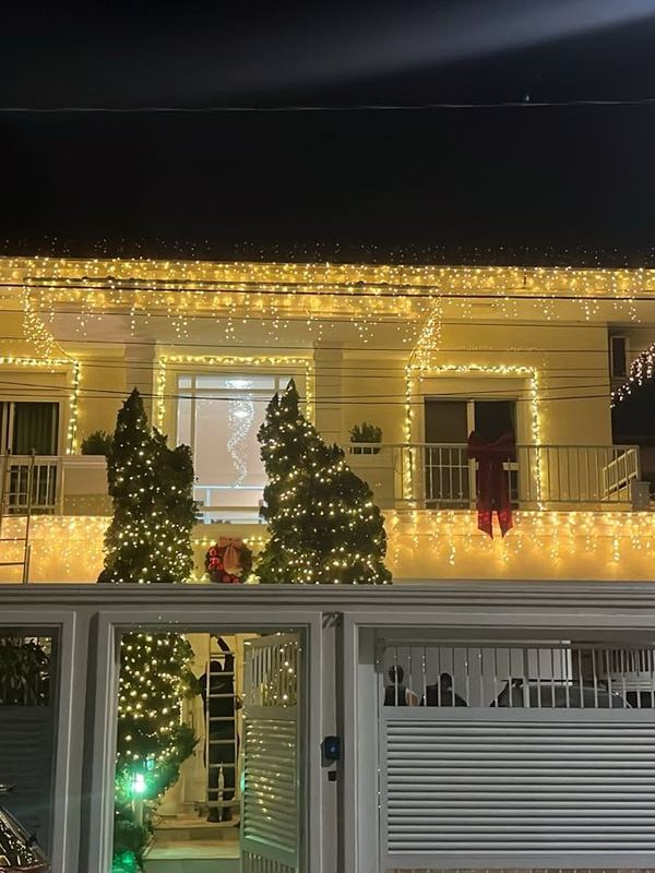 Casa iluminada com cascatas de luz e árvores decoradas na varanda